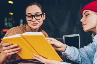 Hipster öğrenci kırmızı şapka gösteren ders kitabı üniversitede ortak eğitim görevde işbirliği sırasında meslektaşım için yararlı bilgiler. Dalgın akıllı gençler birlikte eğitim materyali öğrenme