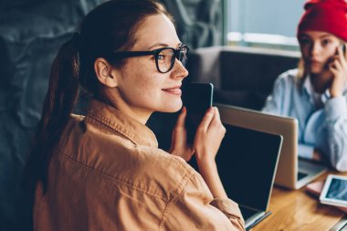 Uzak tutma smartphone elinde seyir ve modern netbook aygıt meslektaşım Smartphone'da söz ederken çalışan mutlu esmer öğrenci. Dizüstü bilgisayarlar kapalı oturan iki kadın serbest
