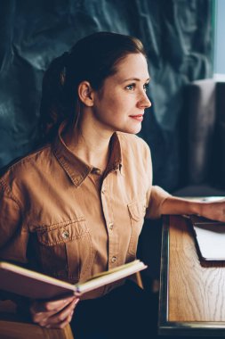 Kitap okuyan ile düşünceli zeki hipster öğrenci dizüstü cihaz oturan ve 4 g kullanarak grafik düzenleri hakkında çalışma elinde kablosuz internet. Modern netbook çalışan genç kadın durulması