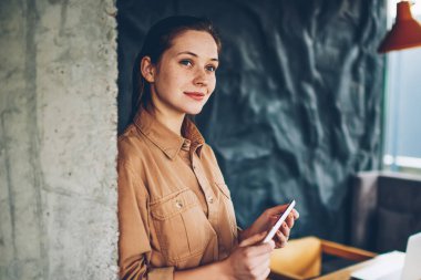 Düşünceli casual kadın blogger modern smartphone tutarak kendi web sitesi geliştirmek için yaratıcı fikirler üzerinde durulması giyinmiş. Planları coworking dururken düşünme düşünce hippi kız