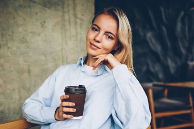 Yarım uzunluk portre sevimli sarışın kadın hipster Blogger lezzetli kahve içecek ve eğlence zamanı kapalı cafeterie iç tadını çıkarırken kameraya gülümseyen şık gömlek giymiş