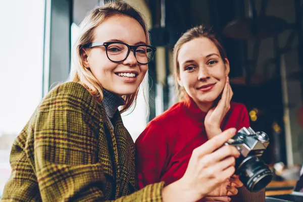 Mutlu yetenekli kadın Amatör kamera şık kahve dükkanında dinlenme olumlu en iyi arkadaşı ile birlikte gülüp, yarı uzunluk portre. Neşeli iki öğrenci ile coworking içinde oturan vintage fotoğraf makinesi