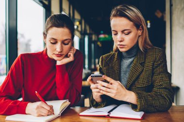 Yetenekli öğrenci test kadın öğretmen Smartphone cep telefonu ile bildirim coworking özel ders sırasında okuma sırasında Not Defteri'nde aşağı yazma. İki hippi kız cep üzerinde internet kullanımı semineri için hazırlanıyor
