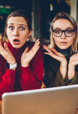 Yarım uzunluk portre karışık iki öğrenci bilgisayarda eğitim sorunu çözmek için bilmiyorum. Coworking yaklaşan sınavlar için hazırlarken kameraya bakarak omuz silkti hipster blogcular şaşkın