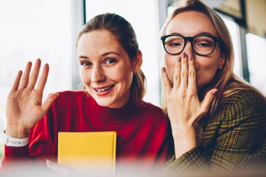 Sallanan el ile neşeli genç kadın ve Sarışın hipster öğrenci hava ile yarım uzunluk portre öpün kameraya gülümseyen. Mutlu güzel blogcular ile birlikte ücretsiz vakit duygusal ifadeler