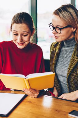 İki başarılı öğrencilere ders kitabı okuma ve birlikte coworking içinde oturan sınava hazırlık sırasında eğitim. Ciddi kadın öğretmen özel ders edebiyat ile iletken olumlu hipster kızla
