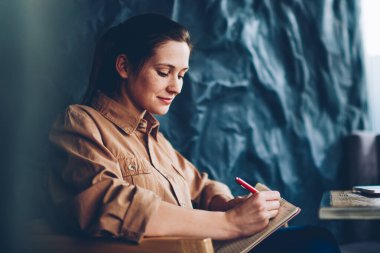 Yaratıcı öğrenci alan coworking içinde boş perde ile modern dizüstü cihaz oturan defter metin bilgileri yazma. Dalgın kadın blogger fikirler netbook çalışma Not Defteri'nde belirterek