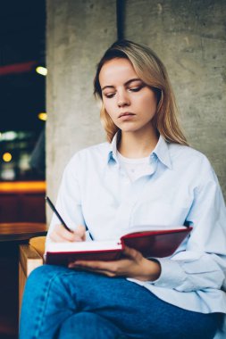 Konsantre öğrenci kayıtları alan coworking içinde boş ekran alanı ile modern dizüstü cihaz oturan ödev Not Defteri'nde aşağı yazma. Dalgın yetenekli genç kadın not defterinde kroki çizim