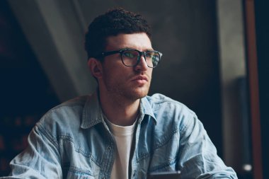 Konsantre olmuş genç hippi adam elinde telefon cihazını tutan ve uygulamayla önemli bir telefon bekliyor. Görme düzeltmesi için gözlüklü düşünceli bir adam. Teknoloji kullanıyor.