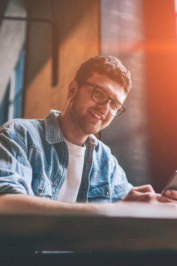 Gözlüklü, cep telefonunu elinde tutan ve kameraya bakan başarılı yeniyetmelerin portresi. Sohbet etmek ve iletişim kurmak için yeni akıllı telefon kullanan, gülümseyen bir ergen.