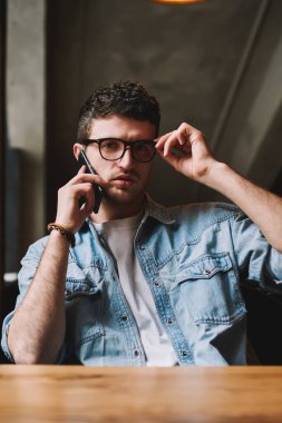 Moda gözlüklü ciddi hippi bir adamın portresi cep telefonundan müşteri hizmetlerini arıyor, kafkasyalı bir adamın içeride kameraya bakarken telefonla konuştuğunu düşünüyor.