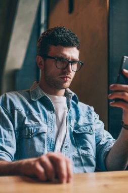 Akıllı telefon tutan ve sosyal haberler okuyan düşünceli bir hippi. Kot pantolonlu genç beyaz bir adam. İçerideki cep telefonundan multimedya uygulamasından izleniyor.