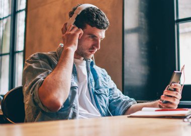 Yakışıklı hippi kablosuz internete girip akıllı telefon cihazından video izliyor dinleme kaydı için elektronik kulaklık kullanıyor, milenyum adamı cep telefonuna medya uygulaması yüklüyor.