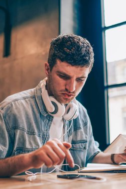 Bluetooth 'a bağlıyken dijital tablet ve akıllı telefon aygıtıyla bilgi paylaşan konsantre hipster adam, cep telefonundan 4G internet ile mesaj okuyan bin yıllık ciddi bir adam.