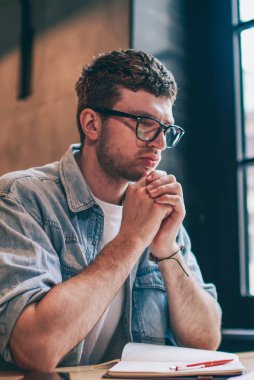 Bulmaca çözme gözlüklü erkek yazar. Masaüstünde oturup makale için fikirler düşünüyor. Düşünceli, kafası karışık hipster çocuk, ders için hazırlanıyor.
