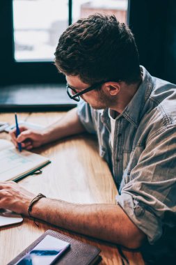 Gündelik giyinmiş hipster çocuk eğitim kitabında bir organizasyon planı yazıyor. Masaüstü bilgisayarında netbook 'la oturuyor, genç adam not defterine kompozisyon yazıyor ve modern teknolojiyle akademi sınavına hazırlanıyor.