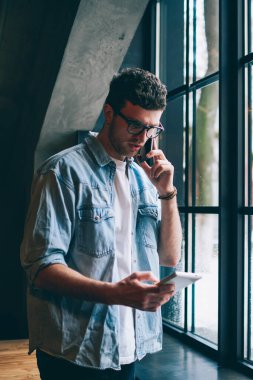 Ciddi hippi adam telefon görüşmesi sırasında hesabı kontrol ediyor dijital tablette ödeme yaparken, e-posta okuyan ve cep telefonuyla iş arkadaşıyla konuşan konsantre bir adam.