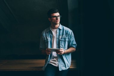 Gündelik görünüşlü düşünceli bir adam elinde dijital tabletle kampüsteki kablosuz internete bağlanmış, hipster adamın bilgi ve mesajlaşma için modern dokunmatik pedi kullandığını düşünüyor.