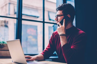 Ciddi bir erkek serbest yazar, modern netbook ile masaüstünde otururken hesap bakiyesini kontrol etmek için operatöre telefon ediyor. Kafeteryaya bağlı dizüstü bilgisayarlı genç hippi.