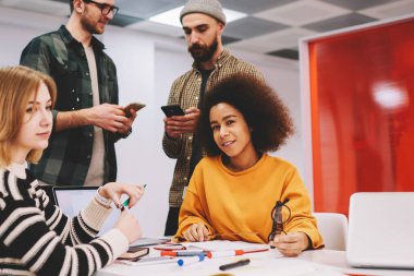 Afrikalı-Amerikalı kadın tasarımcı kamera ile birlikte arkadaşları office Studio'da yeni bina projesi üzerinde çalışırken gülümseyen portresi. Kadın ve erkek öğrenciler üniversitede işbirliği