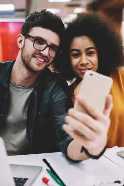 Dijital smartphone ön kamera seyir ve şık coworking uzayda netbooks oturan ekip çalışması sırasında sosyal ağlarda selfie fotoğrafları yayın yapma neşeli en iyi iki arkadaş