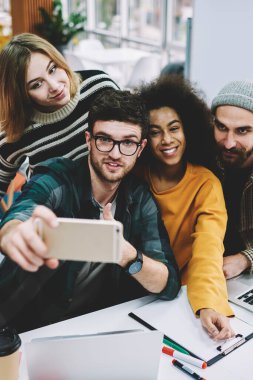 Çok kültürlü grup selfie fotoğrafları netbook Üniversitesi'nde oturan ortak tasarım proje üzerinde iyi bir ekip çalışması sonra modern smartphone yapma şık casual giyim başarılı öğrencinin