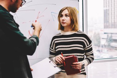 Erkek hoparlör notead ayakta yakınındaki uzay eğitim sesion sırasında coworking içinde Yönetim Kurulu ile öğrenci bilgileri açıklayan. Profesyonel koç atölye eğitim sırasında genç kadın öğretim