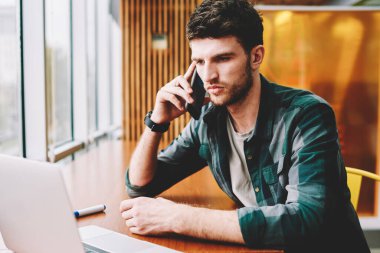 Mobil uygulama ile smartphone üzerinde Web sitesi video izlerken konuşmayı genç yakışıklı erkek Tasarımcısı. Modern cep telefonundan bilgi denetleme sırasında konuşan sakallı adam durulması