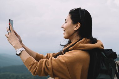Gezide fotoğraf çekmek için cep telefonu kullanan neşeli Asyalı kadın blogcu, tatil turları sırasında konum videosu çeken olumlu milenyum kadın turist