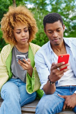 Koyu tenli genç erkek ve kadın sosyal ağlarda modern akıllı telefonlarda 4G interneti kullanarak sohbet ediyorlar. Afrika kökenli Amerikalı erkek ve kadın blogcular telefon cihazlarında uygulamaları güncelliyorlar.