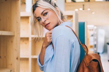 Barcelona 'da üniversite kütüphanesinde kitaplıklar arasında dururken sırt çantalı ve gözlüklü genç bir kadının kameraya baktığı yan bakış.