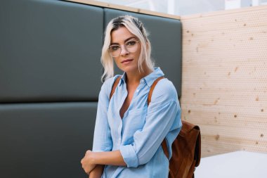 Barcelona 'da üniversite çalışma odasında elinde akıllı bir telefonla kameraya bakan ve masaya yaslanan genç ve çekici bir kız öğrenci.