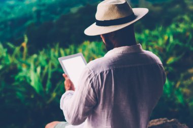 Genç erkek turist dijital göçebe yaz tatilleri boyunca dokunma rampasında çalışıyor. Adam dışarıda otururken tablet üzerinde kitap okuyor. Amazon doğasından esinlenerek.