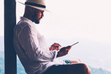Genç erkek turist dijital göçebe yaz tatillerinde dokunmatik ped üzerinde çalışır. Tayland manzarasından esinlenerek açık havada otururken insan sadece tablet üzerinde kitap okuyarak gezer. Teknolojik hareketlilik