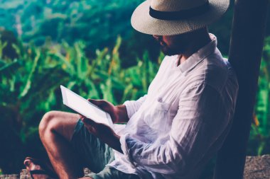 Genç erkek turist dijital göçebe yaz tatilleri boyunca dokunma rampasında çalışıyor. Adam dışarıda otururken tablet üzerinde kitap okuyor. Amazon doğasından esinlenerek.