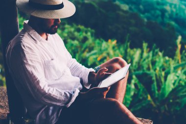 Genç erkek turist dijital göçebe yaz tatilleri boyunca dokunma rampasında çalışıyor. Adam dışarıda otururken tablet üzerinde kitap okuyor. Amazon doğasından esinlenerek.