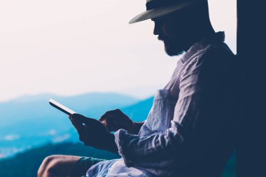 Genç erkek turist dijital göçebe yaz tatillerinde dokunmatik ped üzerinde çalışır. Tayland manzarasından esinlenerek açık havada otururken insan sadece tablet üzerinde kitap okuyarak gezer. Teknolojik hareketlilik