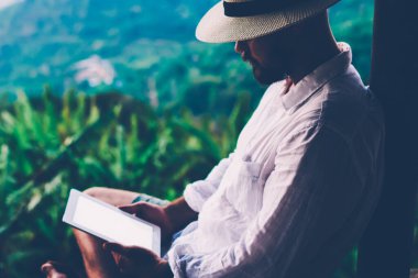 Genç erkek turist dijital göçebe yaz tatilleri boyunca dokunma rampasında çalışıyor. Adam dışarıda otururken tablet üzerinde kitap okuyor. Amazon doğasından esinlenerek.