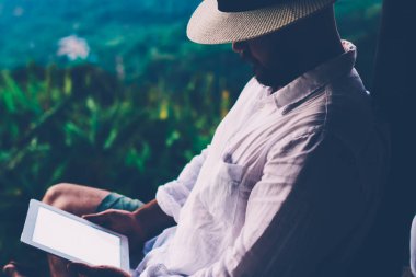 Genç erkek turist dijital göçebe yaz tatilleri boyunca dokunma rampasında çalışıyor. Adam dışarıda otururken tablet üzerinde kitap okuyor. Amazon doğasından esinlenerek.