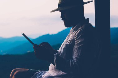 Genç erkek turist dijital göçebe yaz tatillerinde dokunmatik ped üzerinde çalışır. Tayland manzarasından esinlenerek açık havada otururken insan sadece tablet üzerinde kitap okuyarak gezer. Teknolojik hareketlilik