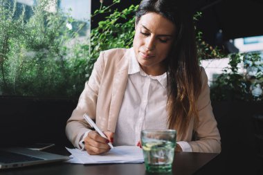 Yayın için gündelik giyinen profesyonel kadın gazeteci dizüstü bilgisayarlı kafe terasında otururken uzaktan iş planlama projesinden memnun gülümseyen iş kadını.