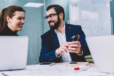 Genç yakışıklı gülümseyen grafik tasarımcı web sayfasında Smartphone cep telefonu ile komik video izlerken çekici kadın meslektaşı ile. Neşeli arkadaşları saygılarımla cep internet sitesinde haber okurken gülmekten