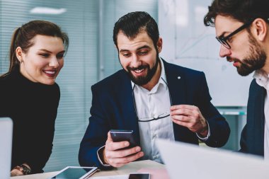 Genç yetenekli gülümseyen iş arkadaşlarınızla birlikte smartphone cep telefonu ile Web sitesi komik video izlerken iyi internet'e bağlı. Grup çalışma molası sırasında eğlenmek akıllı duygusal Mimarlar