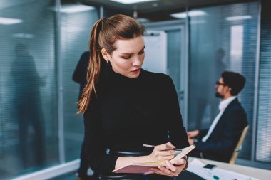 Genç çekici düşünce kadın grafik tasarımcı masada otururken Not defteri için yaratıcı fikirler aşağı yazma formal giyim giymiş. Akıllı kadın çalışan iş sırasında kapalı notlar yapma