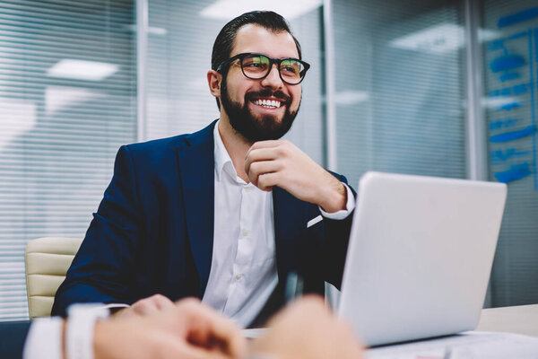Веселый гордый генеральный директор в формальной одежде слушает смешные идеи для нового проекта от коллег во время брифинга в офисе.
