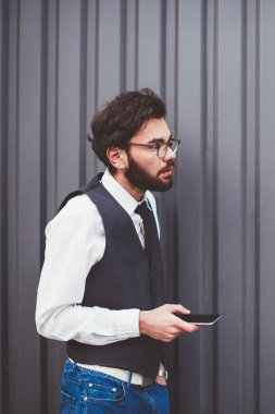 Moda kıyafetli genç adam elinde modern akıllı telefon cihazıyla fotokopi alanının yakınında çağrı bekliyor. Kafkasyalı hippi adam dışarıda mesajlaşmak ve sohbet etmek için yeni cep telefonu kullanıyor.