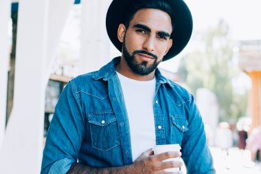 Gündüz vakti cafe terasında dikilirken sıcak içecek ve akıllı telefonuyla kameraya bakan modaya uyan kendine güvenen İspanyol serbest yazar.