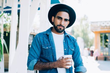 Gündüz vakti cafe terasında dikilirken sıcak içecek ve akıllı telefonuyla kameraya bakan modaya uyan kendine güvenen İspanyol serbest yazar.