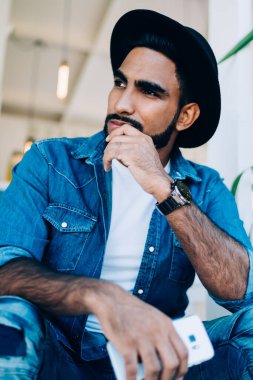 İspanyol kökenli, düşünceli, kot elbiseli ve şapkalı sakin bir erkekten. Elinde cep telefonuyla teras merdivenlerinde uzanmış başını çeviren bir şapkayla.