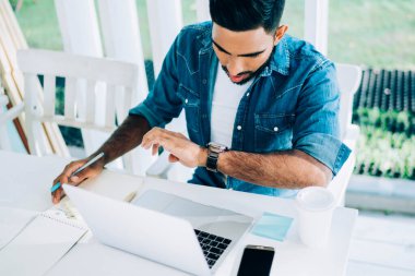 Yukardan gelen çalışkan İspanyol erkek bilek saatine odaklanmış ve karar verirken netbook, akıllı telefon ve güneşli bir yaz gününde terasta not defterine yazı yazarak şaşırdı.